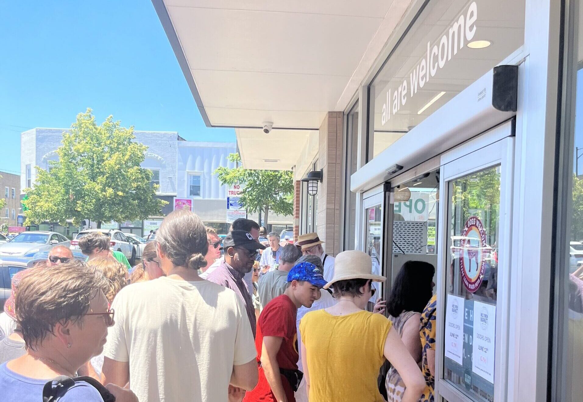 A group of people standing in line outside of a grocery store entrance.