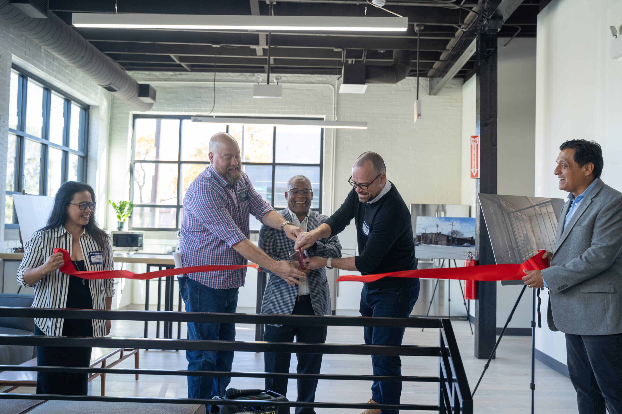 Three men cutting a red ribbon in a ceremony.